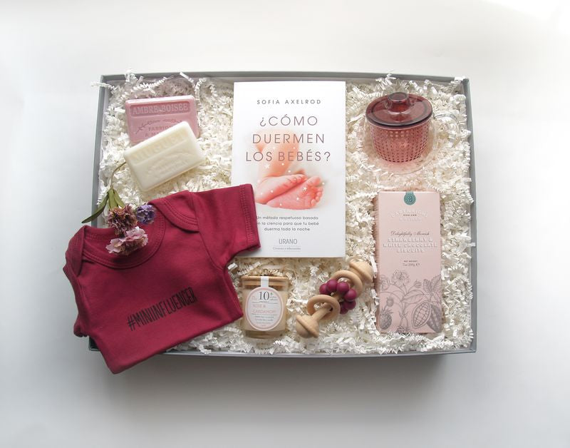 Caja de regalo con varios productos únicos como un body para bebé, sonajero y otros productos para el bebé.